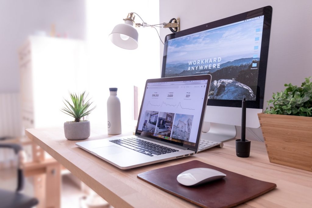 A large screen and laptop sitting on a desk. Tools of a virtual assistant.